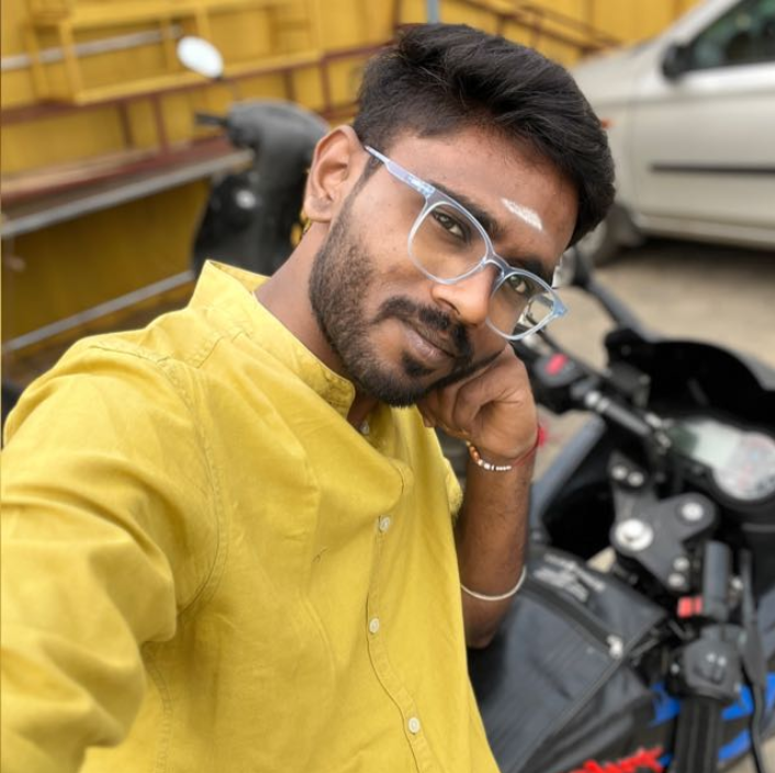 A man wearing glasses and a bright yellow shirt smiles as he takes a selfie.